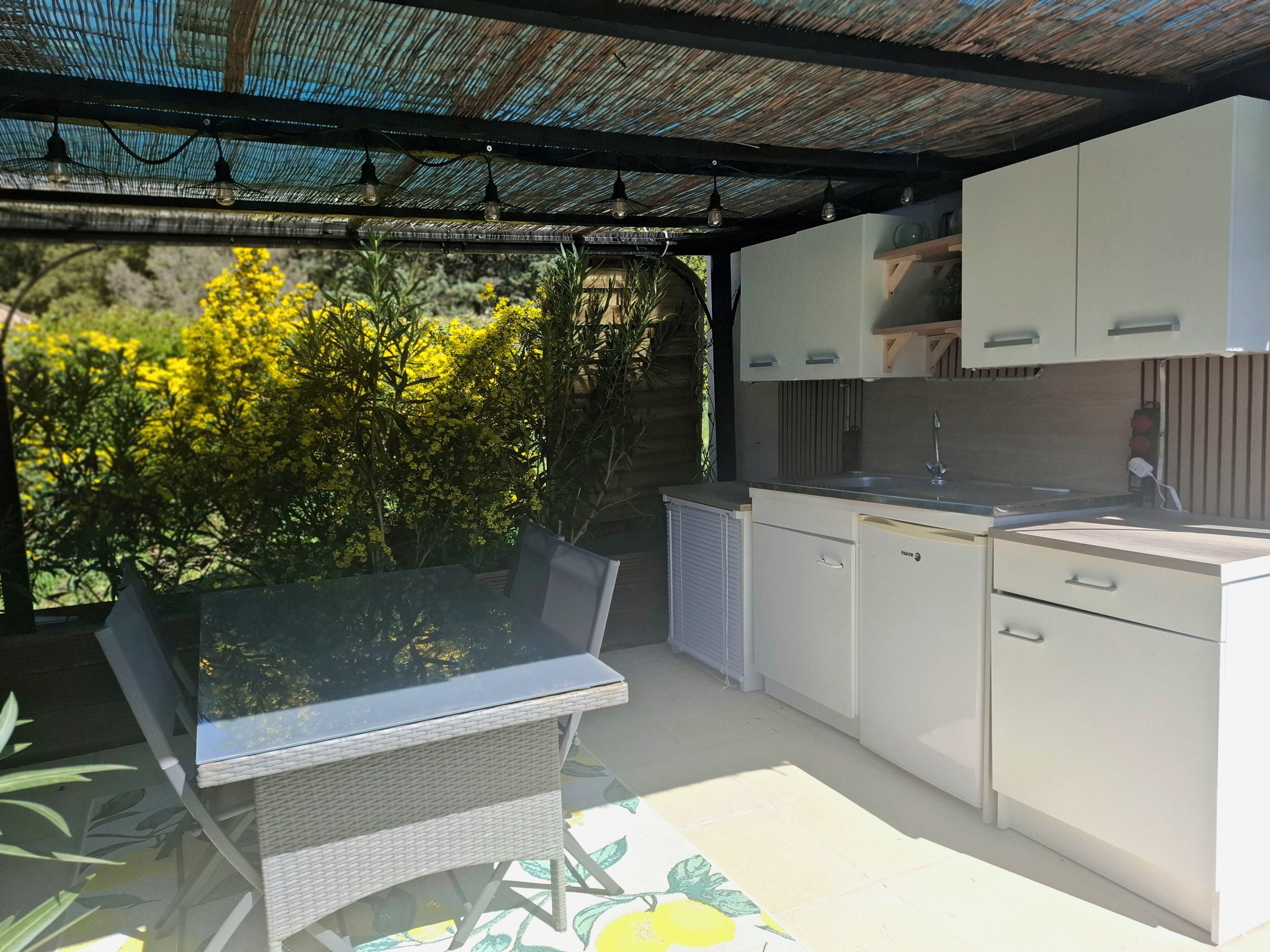 Cozinha moderna com armários brancos, uma mesa de jantar de vidro e vista para o verde.