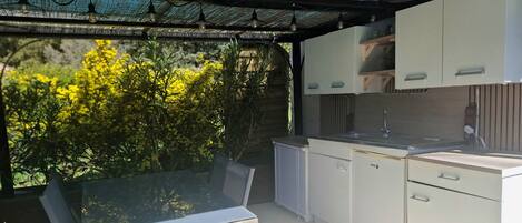 Cozinha moderna com armários brancos, uma mesa de jantar de vidro e vista para o verde.