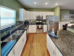 A modern kitchen with white cabinets, a stainless steel refrigerator, a microwave, and a stove. - Fin and Feather (Port Aransas)