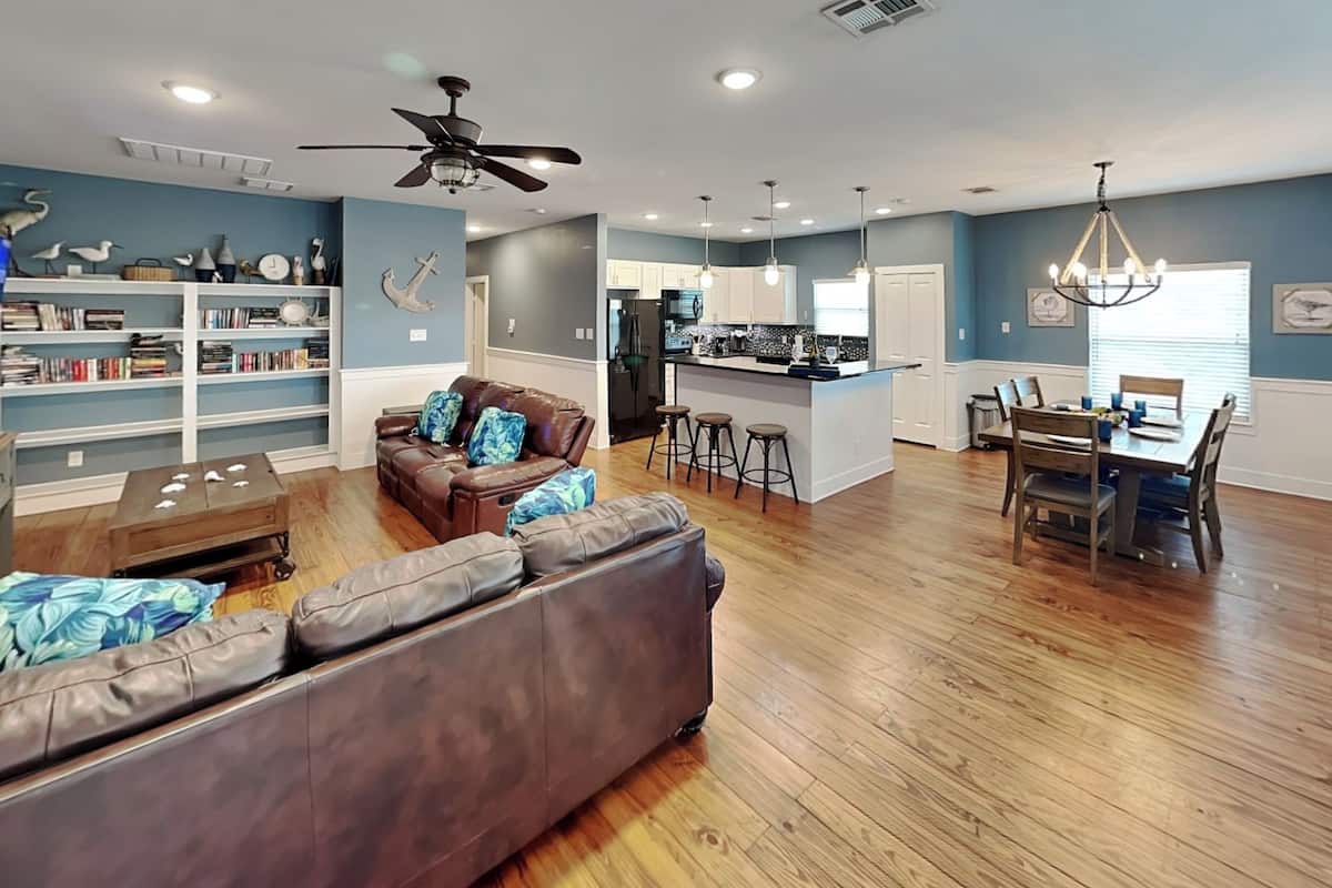 A spacious living area with a sofa, a coffee table, a bookshelf, a dining area with a table and chairs, and a kitchen with a bar.