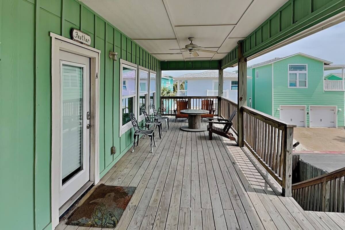 A covered porch with a table and chairs, a door labeled 'Feather,' and a view of a green building.