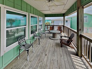 A covered porch with a wooden floor, metal chairs, a round table, and a ceiling fan. - Fin and Feather (Port Aransas)