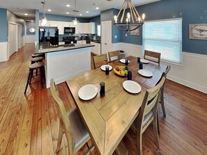 A modern kitchen with white cabinets, a central island, and a dining area with a wooden table set for four. - Fin and Feather (Port Aransas)