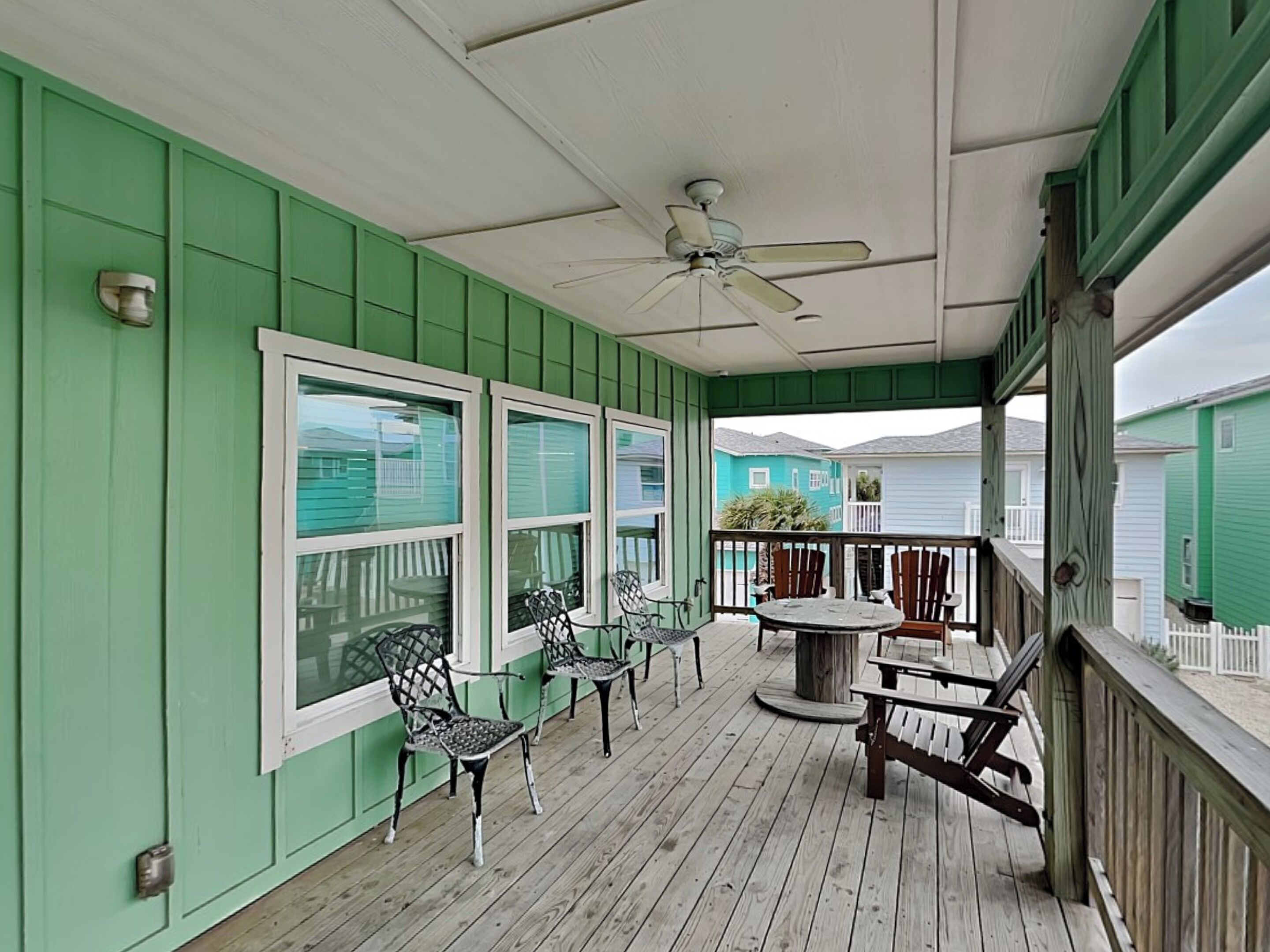 A covered porch with green walls, a ceiling fan, and outdoor furniture.