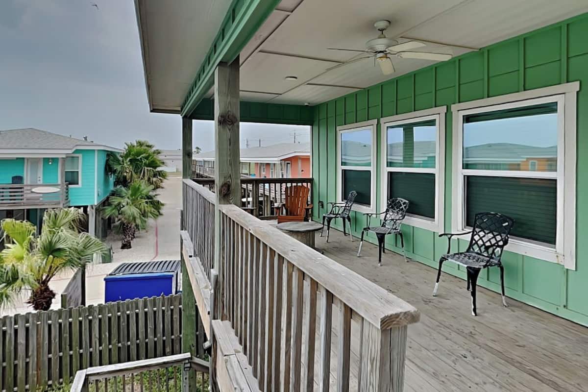 A covered outdoor deck with a railing, a ceiling fan, and a view of neighboring houses.