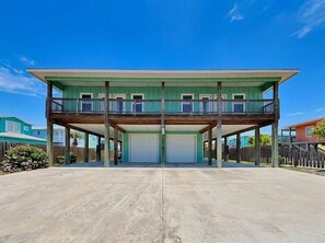 A two-story building with a balcony on the upper floor, a garage door, and a concrete driveway. - Fin and Feather (Port Aransas)
