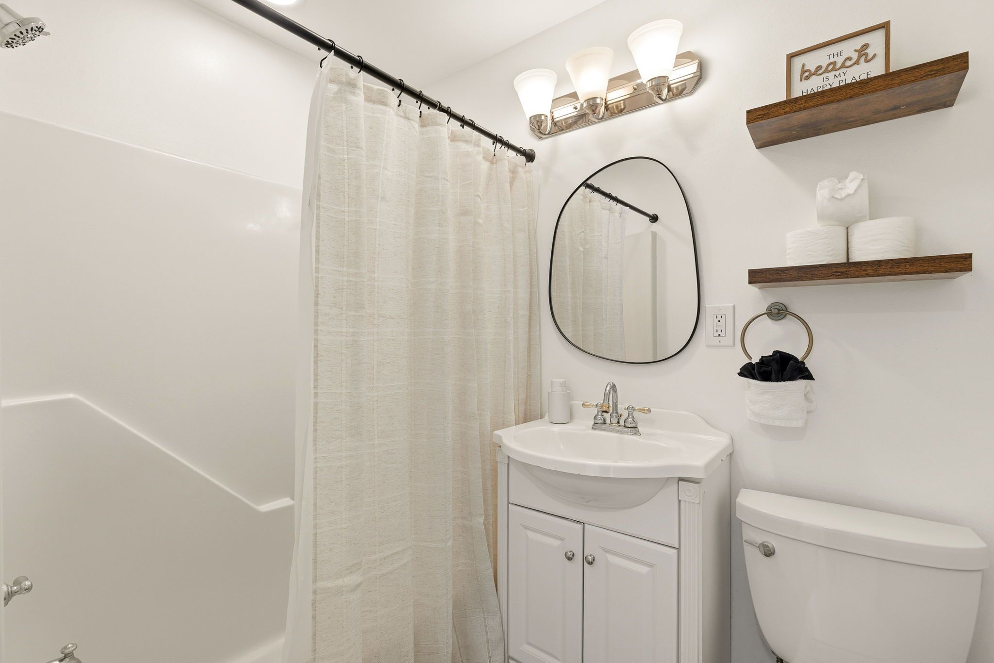 A bathroom with a bathtub, a sink, a toilet, a shower curtain, a mirror, and a shelf with towels.