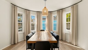 Un comedor con una mesa de madera, sillas negras, cortinas color beige y una lámpara colgante.