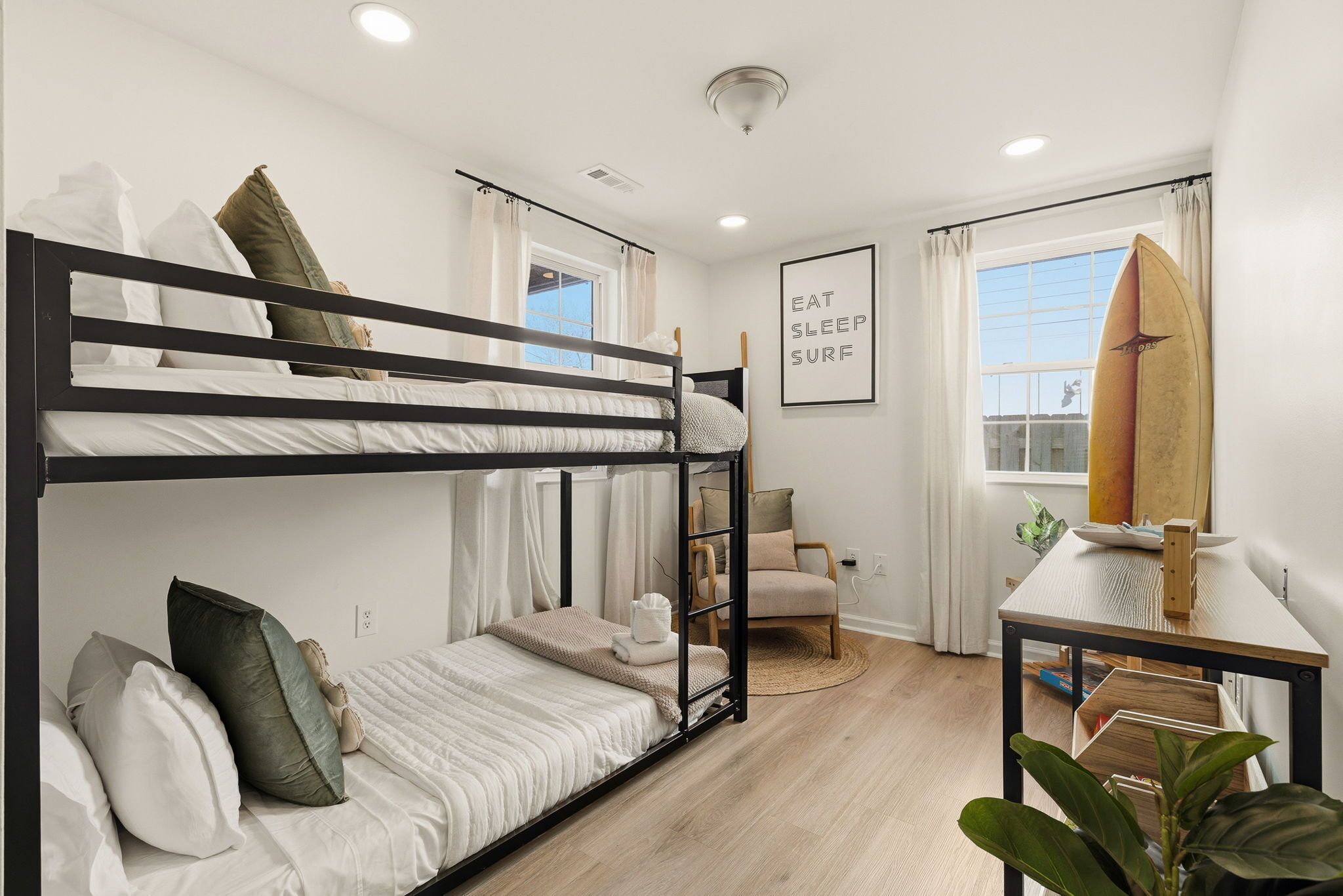 A bunk bed room with a window, a surfboard, a chair, and a framed sign.