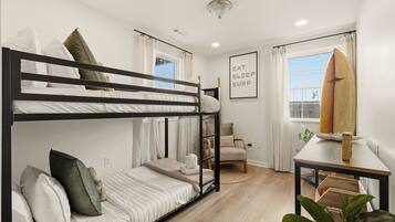 A bunk bed room with a window, a surfboard, a chair, and a framed sign.