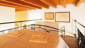 Un dormitori amb un llit, un sostre de fusta, un taulell blanc i dos quadres al mur.