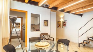 Un espai de vida modern amb una taula de dinar de vidre envoltada de cadires, una zona de cuina i una escala.