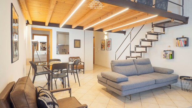 Un saló modern amb un sofà, cadires, zona de menjador i una escala.