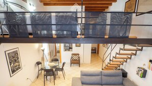 Un interior modern amb un balcó de vidre, una zona de menjador, un sofà i una escala.