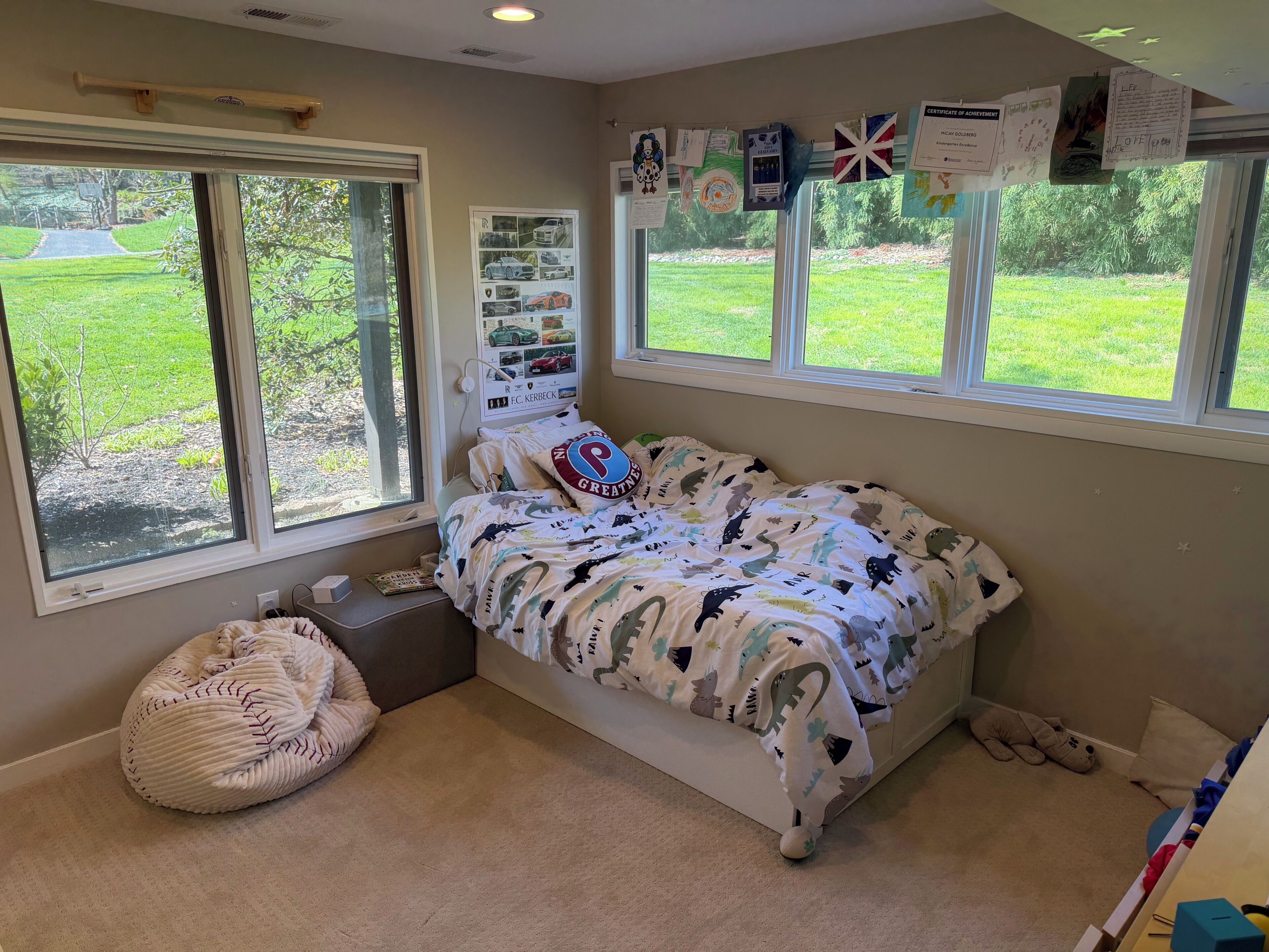 A bedroom with a bed, a bean bag, a window, and a wall with certificates.