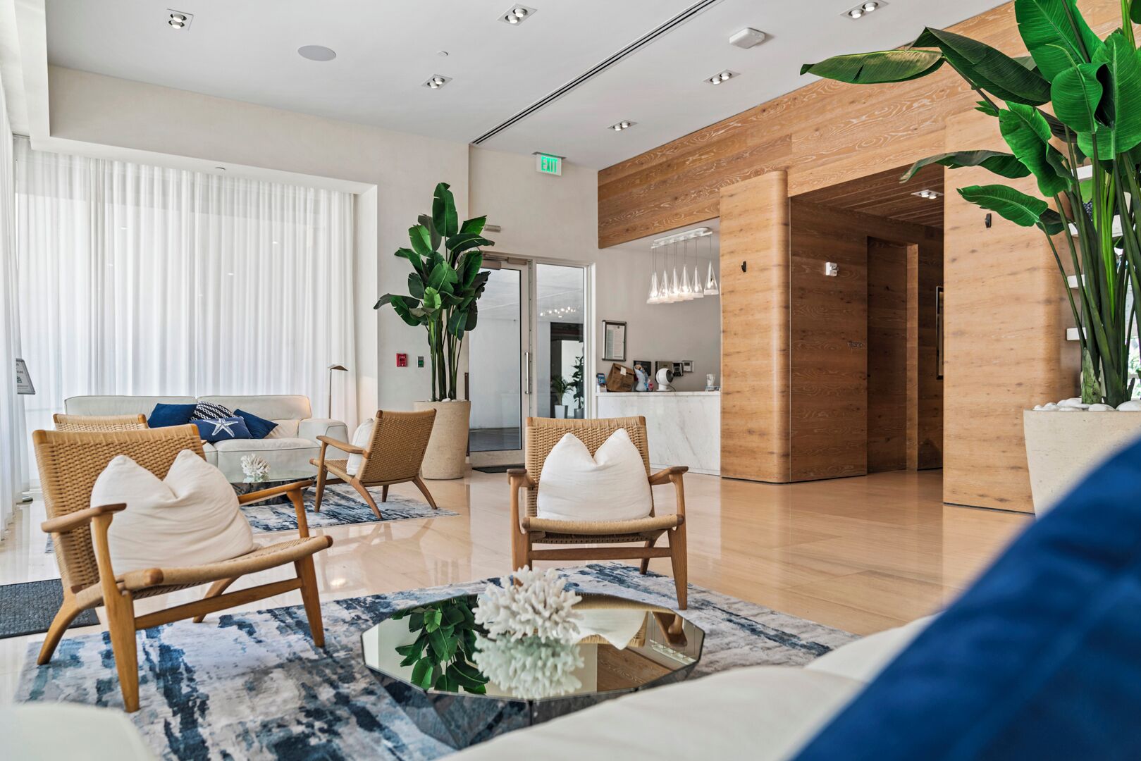 A modern hotel lobby with wicker chairs, a marble coffee table, and a large potted plant.
