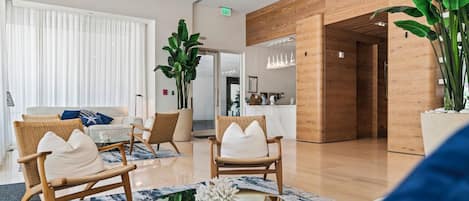 A modern hotel lobby with wicker chairs, a marble coffee table, and a large potted plant.