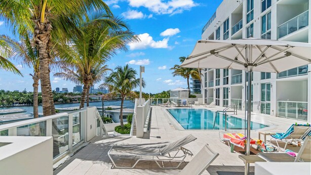 A rooftop pool with lounge chairs and umbrellas, surrounded by palm trees and a city skyline. - 2 Bed/3 Bath Beach Townhouse  I 1600sqft I 5 Star amenities I No Resort fee I (Fort Lauderdale)