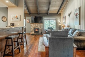 A living room with a fireplace, a sofa, a bar area with stools, and a television. - Elevated Alpine Retreat Near Canyon Lodge 643 (Mammoth Lakes)