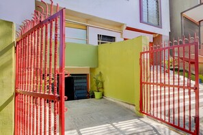 A gated courtyard with a potted plant, a metal gate, and a building with a window. - Classic Hotel Four Square (Patna)