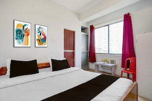 Une chambre d’hôtel avec un lit, deux œuvres d’art encadrées, une fenêtre avec des rideaux, un bureau et une chaise.