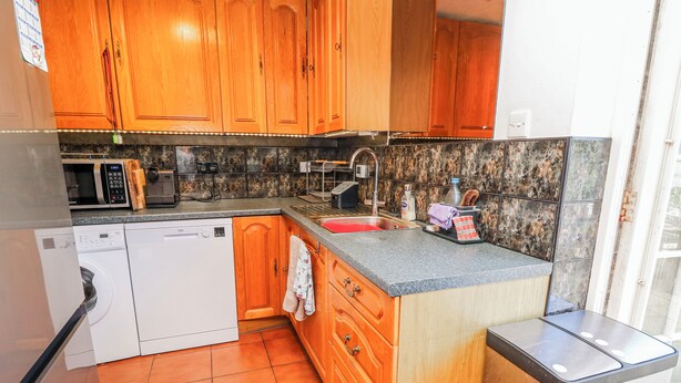 A kitchen with wooden cabinets, a dishwasher, a microwave, and a sink. - 2 Trelawny Way (Bembridge)