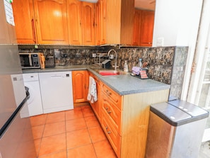 A kitchen with wooden cabinets, a dishwasher, a microwave, and a sink. - 2 Trelawny Way (Bembridge)