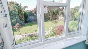 A window with a view of a garden, a white window frame, and a curtain with sailboat patterns. - 2 Trelawny Way (Bembridge)
