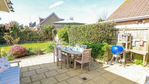 A patio with a table and chairs, a barbecue grill, and a garden with various plants and a hedge. - 2 Trelawny Way (Bembridge)