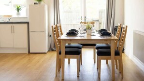 Un comedor con una mesa de madera dispuesta para cuatro personas, rodeada de sillas con cojines negros.