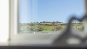 Vista a través de una ventana de un paisaje rural con colinas ondulantes, cielo despejado y algunas construcciones dispersas.