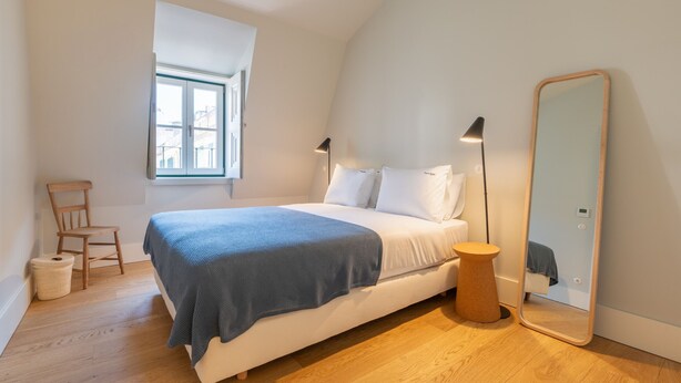 Ein Schlafzimmer mit Bett, Nachttisch, Stuhl, Lampe, Spiegel und Fenster.