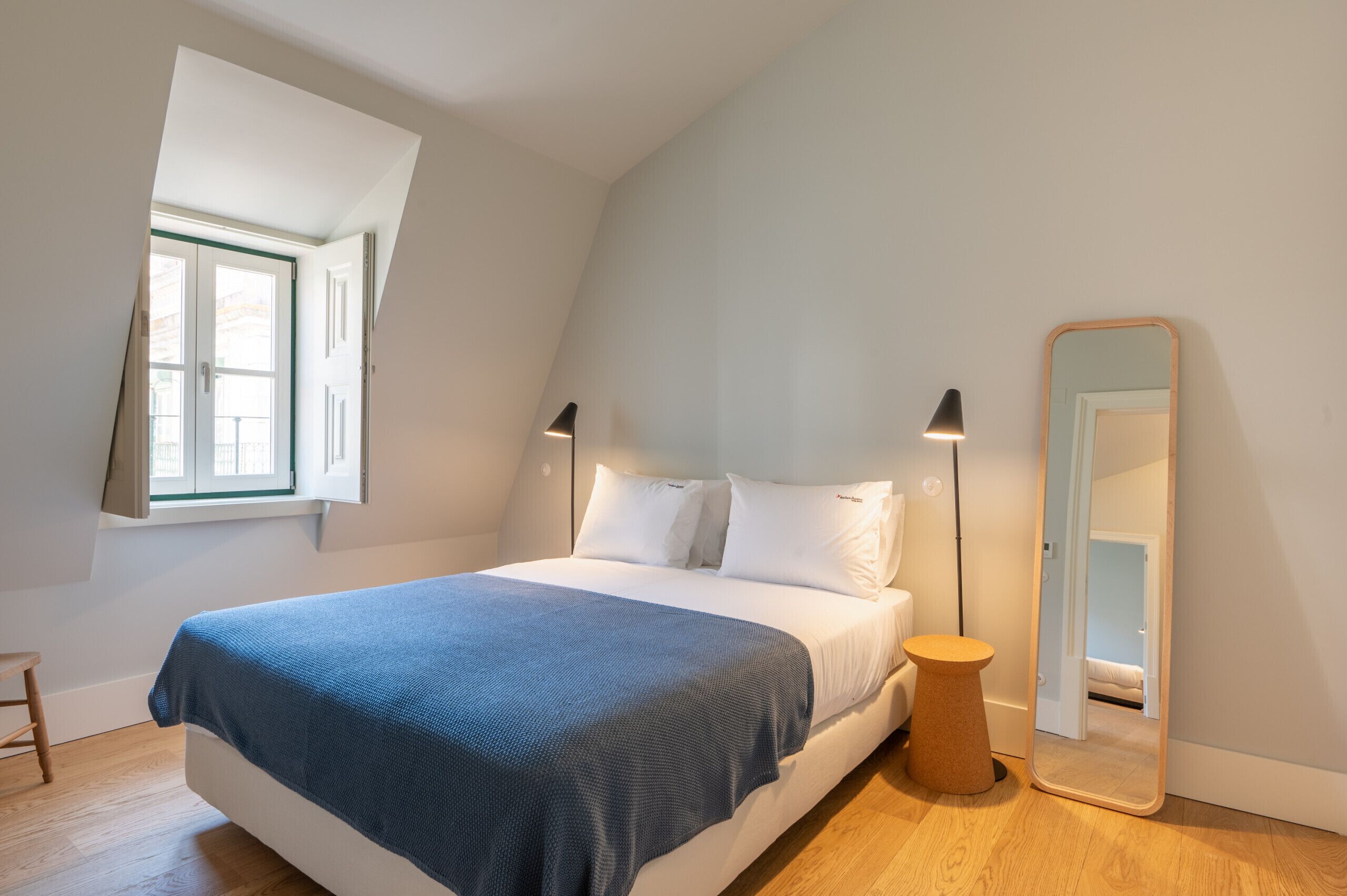 Ein Schlafzimmer mit einem Bett, einem Nachttisch, einem Spiegel und einem Fenster.
