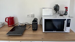 A kitchen counter with a microwave, toaster, induction cooktop, and a red coffee maker. - Sea and mountain view studio, new and comfortable (Saint-Paul)