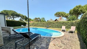 Una piscina con sillas de descanso, suelo de piedra y una cadena para colgar objetos.