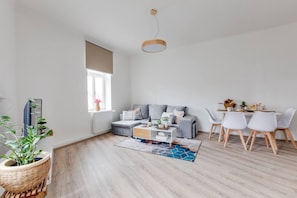 Ein modernes Wohnzimmer mit einem grauen Sofa, einem Couchtisch und einem Essbereich mit weißen Stühlen.