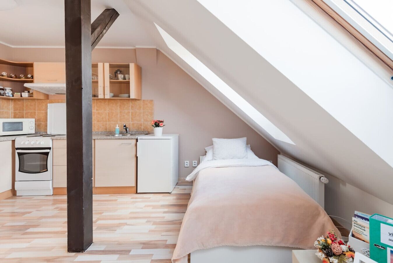 A compact bedroom with a bed, a small kitchenette, and a sloped ceiling.