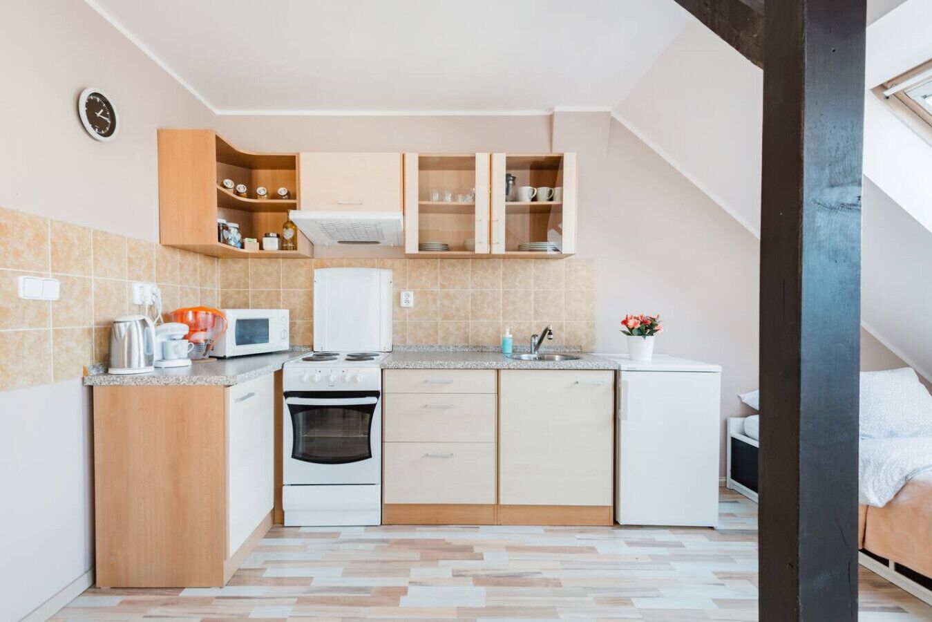Una cocina compacta con microondas, estufa y armarios, un lavamanos pequeño y un reloj en la pared.