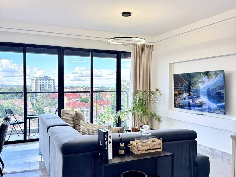 Un salón moderno con un sofá negro, una mesa de centro y un amplio ventanal con vistas a la ciudad.