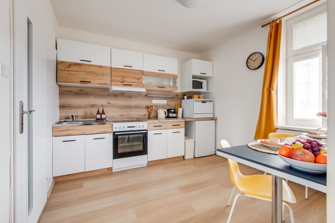 Cozinha compacta com armários brancos, bancada de madeira, micro-ondas, fogão e área de refeições com mesa e cadeiras.