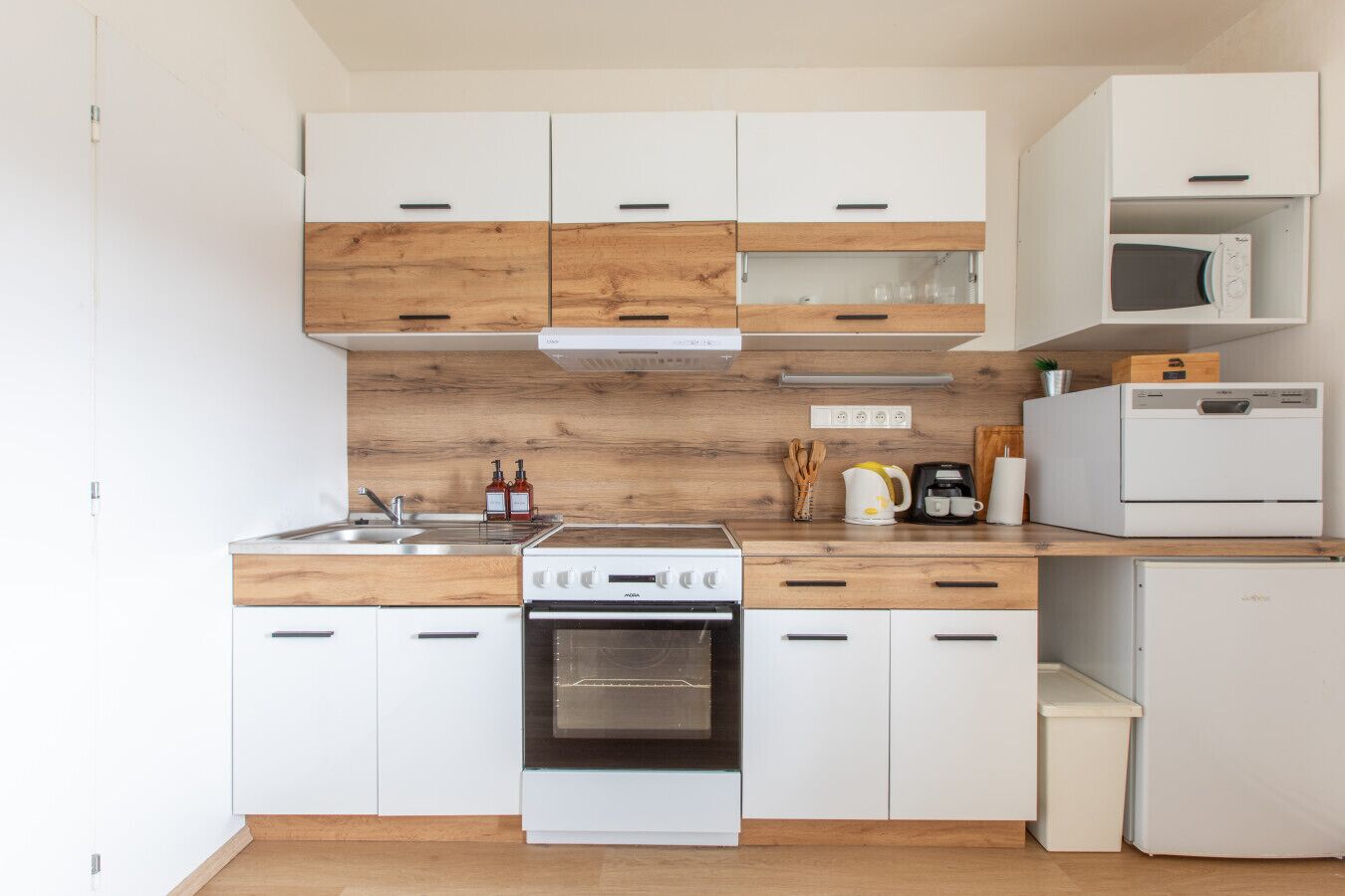 A modern kitchen with white cabinets, a wooden backsplash, a stove, a microwave, and a refrigerator.