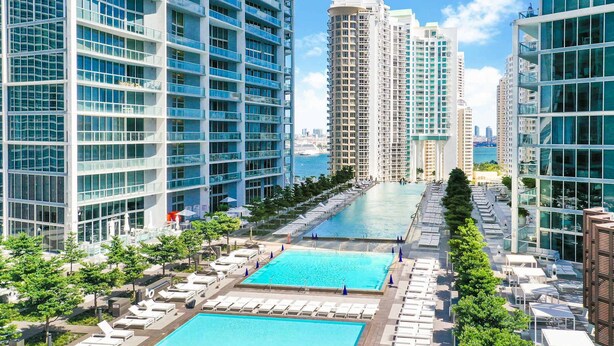 Un hotel moderno con múltiples piscinas, zonas de estar al aire libre y vistas al horizonte de la ciudad.