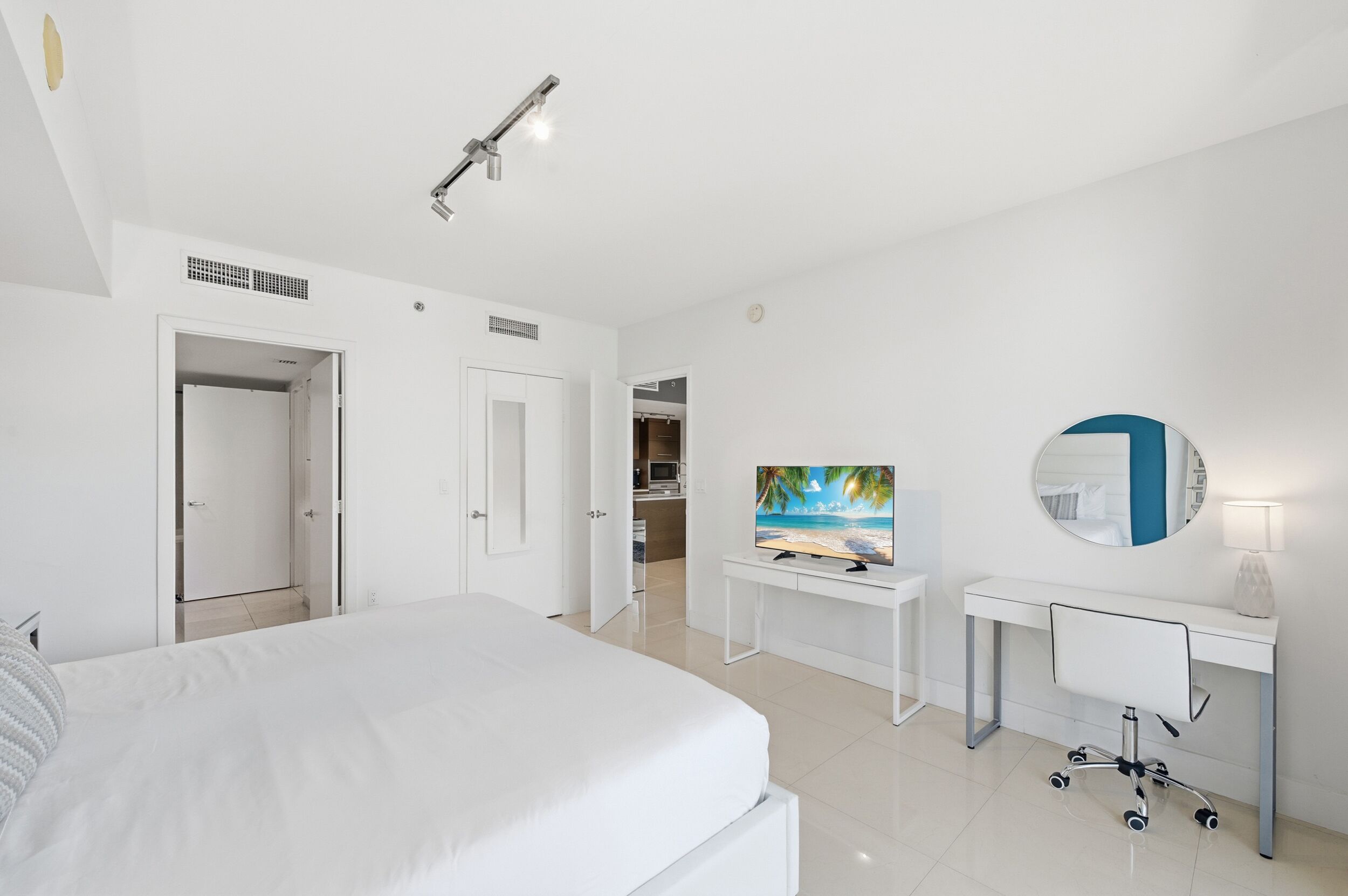 A modern hotel room with a large bed, a desk with a computer, a TV, and a mirror.