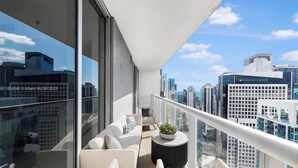 Un balcón con vista a la ciudad, un sofá, una mesita y una planta en maceta.