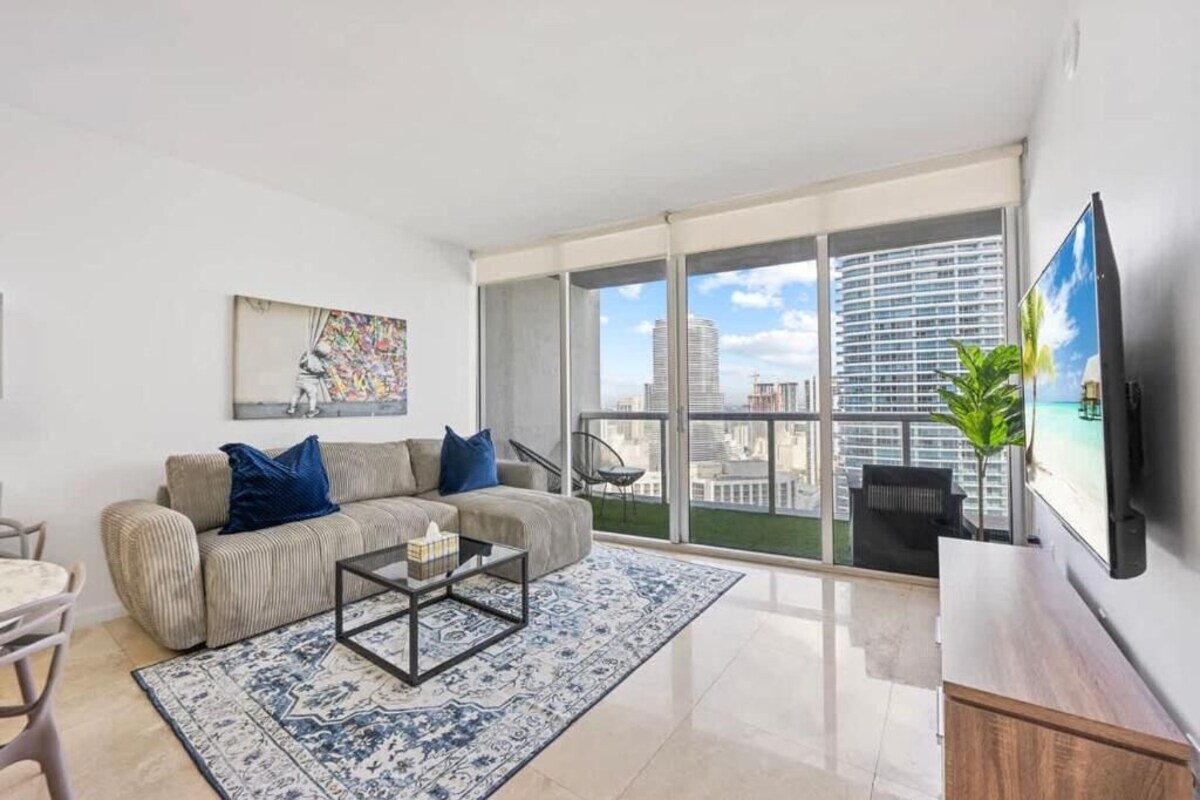Uma sala de estar moderna com sofá, mesa de centro e uma grande janela com vista para a cidade.
