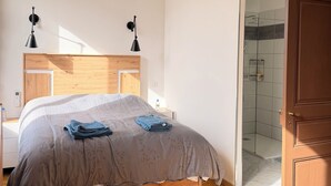 A bedroom with a wooden bed, two bedside lamps, a ceiling light, and a glass shower door. - Air-conditioned house with terrace and elevator (Lauzerte)