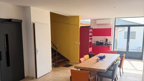 A dining area with a table and chairs, a kitchen in the background, and a staircase leading to another level. - Air-conditioned house with terrace and elevator (Lauzerte)