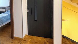 A hallway with a black door, wooden flooring, and a bed with a blue and white checkered bedspread in the background. - Air-conditioned house with terrace and elevator (Lauzerte)