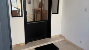 A room with a black-framed door, a small wooden cabinet, a framed picture on the wall, and a black doormat on the floor. - Air-conditioned house with terrace and elevator (Lauzerte)