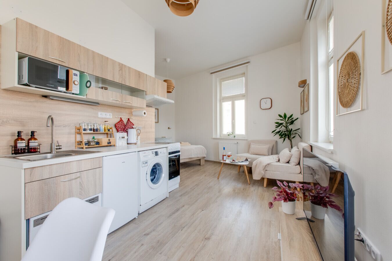 A modern kitchen with a washing machine, a dining area with a table and chairs, and a living area with a sofa.
